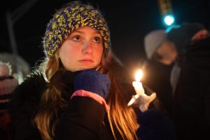 Teenage girl in hat holds a lighted candle at a vigil for those killed and wounded at the Oxford High School shooting.